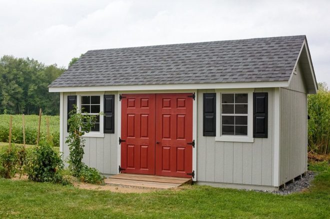 Grey A Frame shed, with white trim and red doors, next to a garden.
