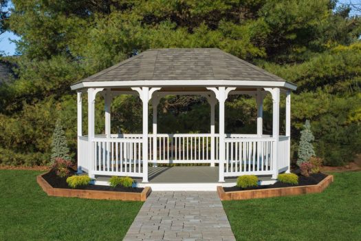 White oval gazebo with a stone brick pathway and a narrow garden surrounding it.