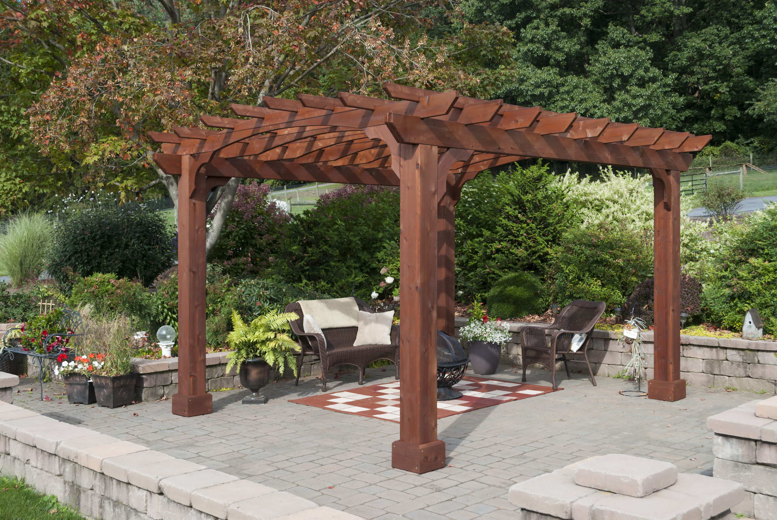 A moderate sized wooden pergola on a stone patio beside a garden.
