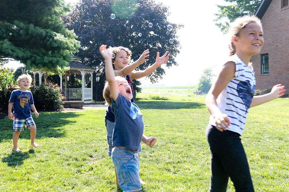 Children playing with bubbles in backyard near wooden DIY gazebo kit creating family memories